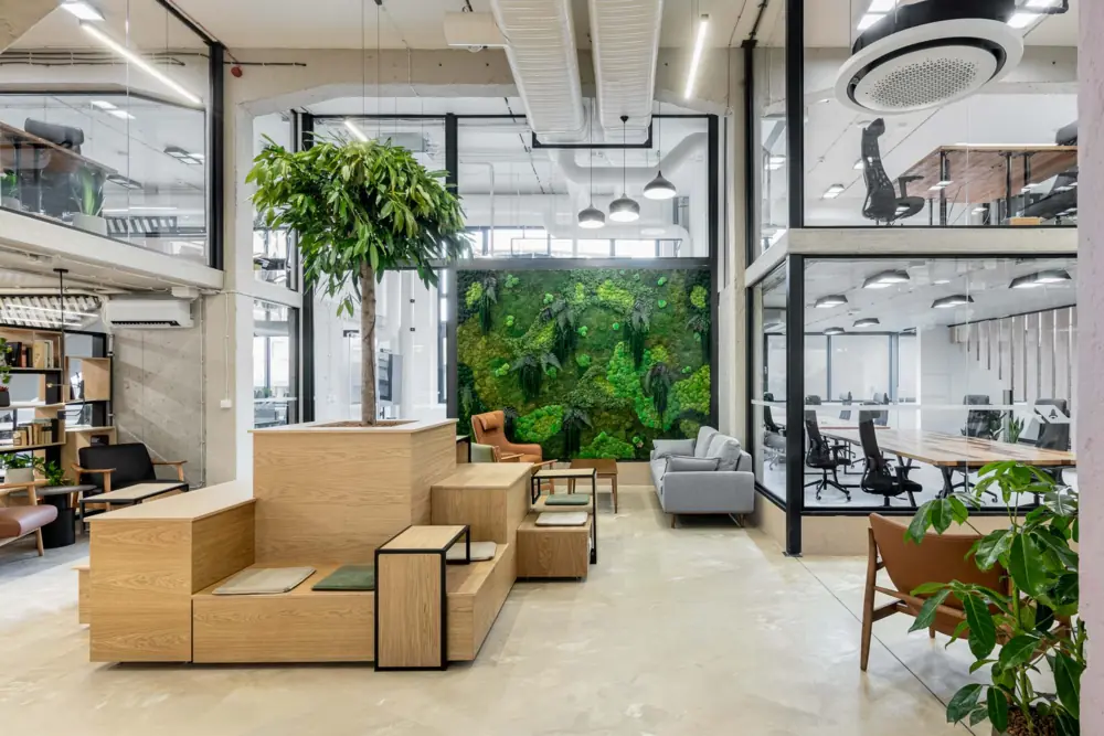 Multi-level lounge at Puzl CowOrKing with stepped wooden seating, sofas, a green wall and glass offices