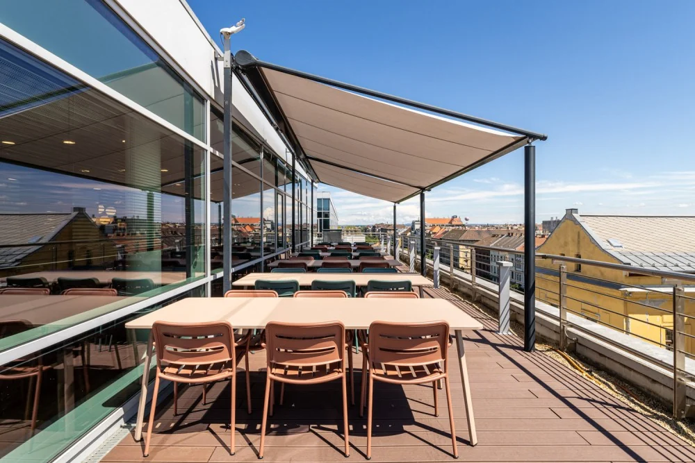 Sixth-floor terrace with long tables, chairs and views over the city rooftops